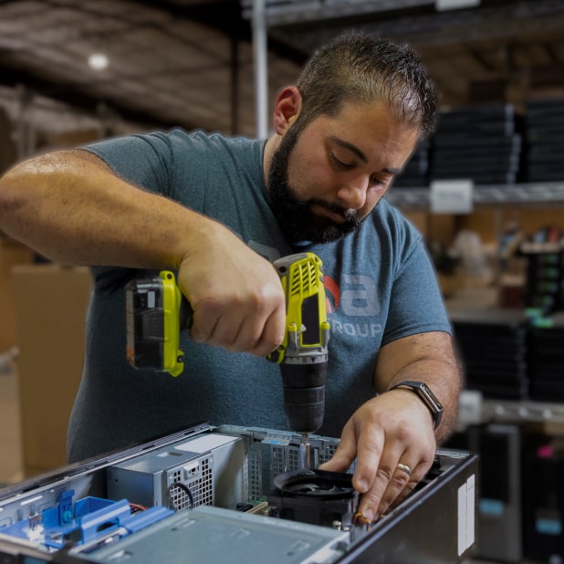 Man using a drill to disassemble a computer in a warehouse